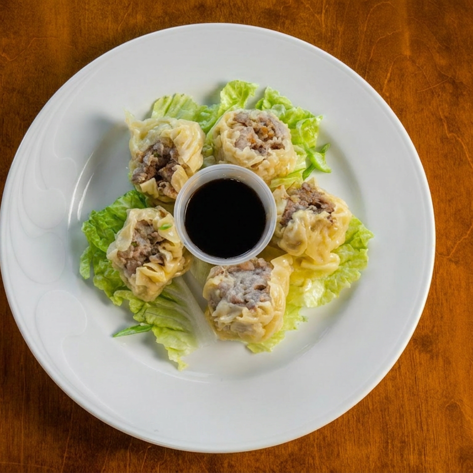 Four steamed dumplings arranged on lettuce around a bowl of dark dipping sauce on a white plate.