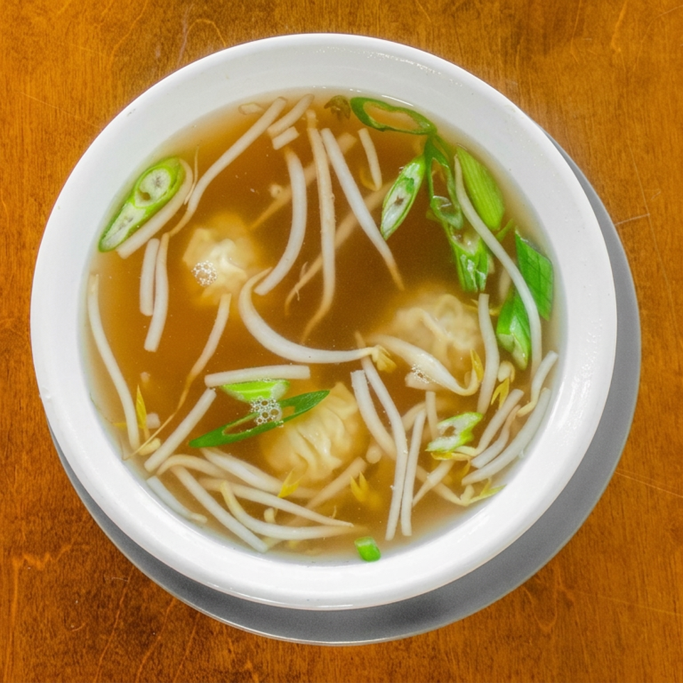 Top-down view of clear noodle soup with dumplings, bean sprouts, and sliced green onions in a white bowl on a wooden table.
